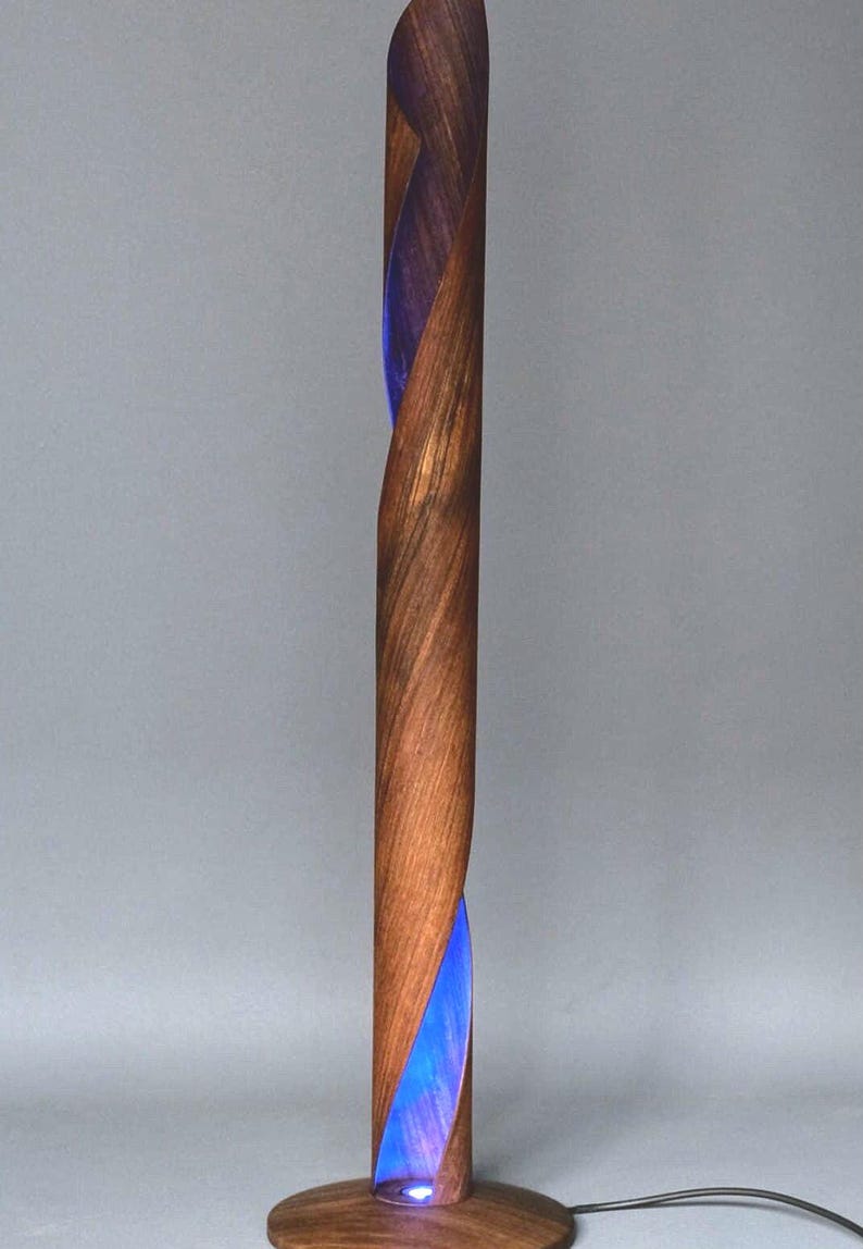 A wooden floor lamp with a blue light shining through a gap in the wood. The lamp is made of a twisted piece of wood and has a round base.