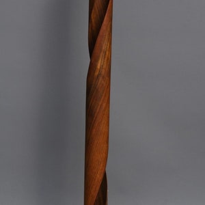A wooden floor lamp with a twisted, cylindrical base and a round, wooden base. The lamp has a black cord and plug.