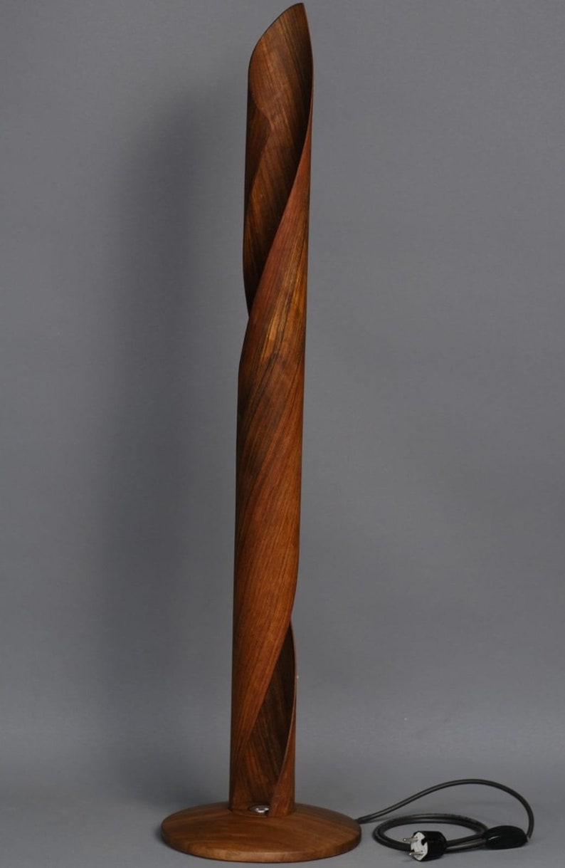A wooden floor lamp with a twisted, cylindrical base and a round, wooden base. The lamp has a black cord and plug.