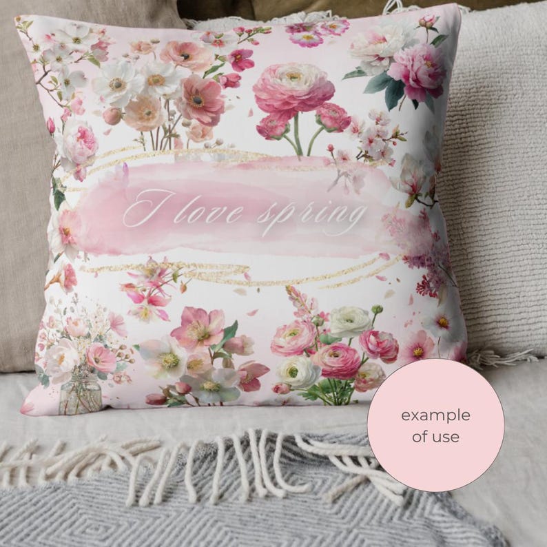 May include: A decorative pillow with a floral design. The pillow features a watercolor-style print of pink and white flowers, with the words "I love spring" in the center. The pillow is surrounded by other pillows and a blanket.
