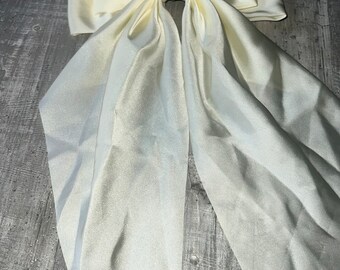 May include: A large, white satin bow with long tails. The bow is tied in a knot and the tails are flowing down.