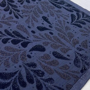 May include: A close-up shot of a navy blue fabric featuring a repeating pattern of stylized leaf shapes. The leaves are a darker navy with a velvet texture and are embellished with tiny, sparkling silver dots. The background is a solid navy blue.
