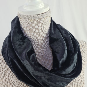 May include: A dark green velvet infinity scarf displayed on a white mannequin head. The scarf's deep colour and soft texture are prominent. The mannequin is set against a white backdrop.