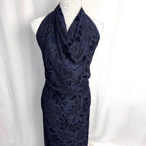 May include: A navy blue halter dress with a floral pattern. The dress has a cowl neckline and a fitted waist. The fabric has a subtle sheen, and the dress is displayed on a mannequin.