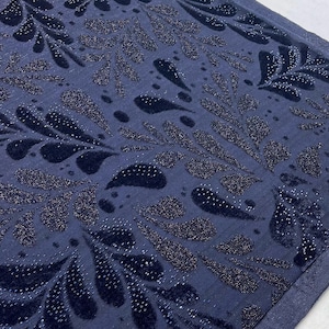 May include: A close-up shot of a navy blue fabric featuring a repeating pattern of stylized leaf shapes. The leaves are a darker navy with a velvet texture and are embellished with tiny, sparkling silver dots. The background is a solid navy blue.