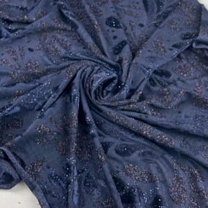 May include: Dark blue fabric with a velvet texture and a swirling pattern. The fabric features scattered sequins and a darker, textured design. This luxurious, shimmering textile is suitable for clothing or home decor projects.