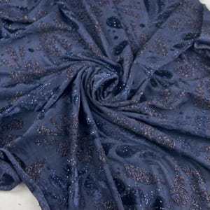 May include: Dark blue fabric with a velvet texture and a swirling pattern. The fabric features scattered sequins and a darker, textured design. This luxurious, shimmering textile is suitable for clothing or home decor projects.