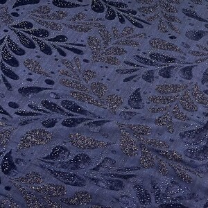 May include: Close-up of a navy blue fabric featuring a repeating pattern of stylised leaves. The leaves are embellished with glitter, creating a shimmering effect. The fabric has a textured appearance, with subtle vertical lines.