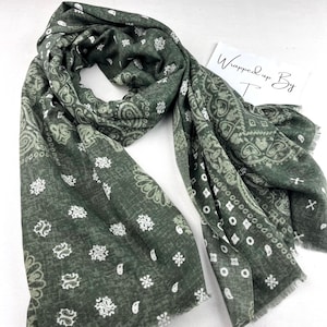 Könnte beinhalten: Ein dunkelgrüner Schal mit Paisley-Muster und weißen floralen Akzenten. Der Schal ist drapiert und zeigt seine weiche Textur und sein Design. Der Text "Wrapped up By T" ist auf einer Karte zu sehen.