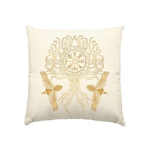 Peut inclure: Un coussin carré blanc cassé avec une impression graphique dorée. Le motif représente un arbre central aux branches et racines détaillées, un symbole Vegvisir circulaire entouré de runes et deux oiseaux symétriques en plein vol.