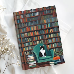 May include: A rectangular notebook featuring a printed illustration of a black and white cat sitting in a teal armchair. The background shows a tall wooden bookshelf filled with colourful books, with stacks of books on the floor near the chair.