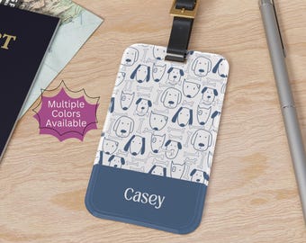 May include: A rectangular luggage tag with a dog and bone pattern in white and navy blue. The bottom section is solid navy blue with the name "Casey" printed in white. The tag has a black leather strap and gold buckle.