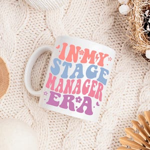May include: White ceramic mug with a pink, blue and purple design that says "In My Stage Manager Era".