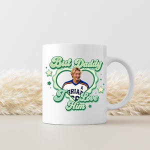 Puede incluir: Taza de cer&aacute;mica blanca con un dise&ntilde;o verde y blanco que dice "But Daddy I Love Him". El dise&ntilde;o incluye una imagen en forma de coraz&oacute;n de una persona con una camiseta. La taza tiene un asa blanca.