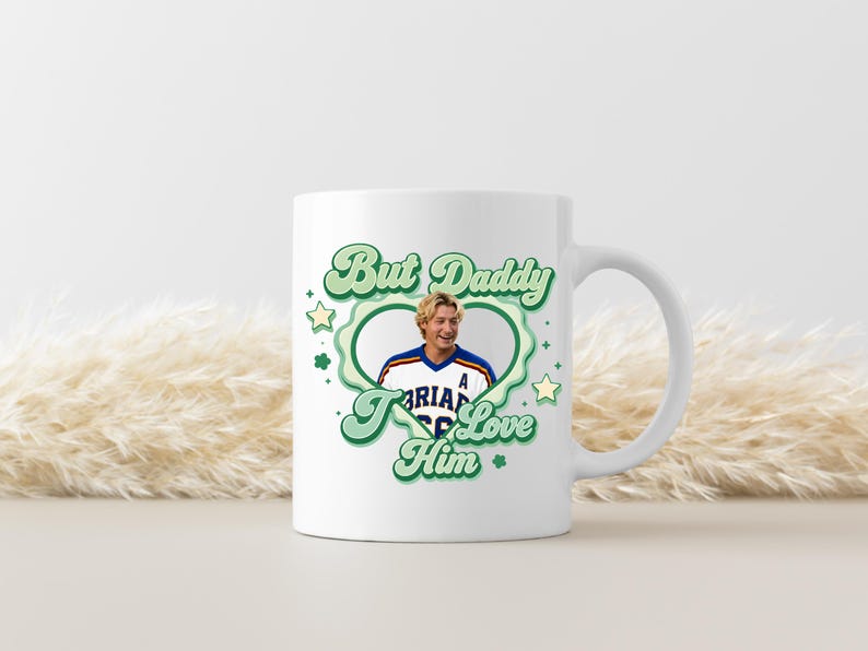 Puede incluir: Taza de cer&aacute;mica blanca con un dise&ntilde;o verde y blanco que dice "But Daddy I Love Him". El dise&ntilde;o incluye una imagen en forma de coraz&oacute;n de una persona con una camiseta. La taza tiene un asa blanca.