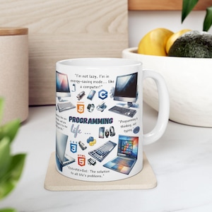 May include: White ceramic mug with a colourful design featuring various programming languages, code snippets, and related icons. The text on the mug reads "I'm not lazy, I'm in energy-saving mode... like a computer!" and "Programming is thinking, not typing."