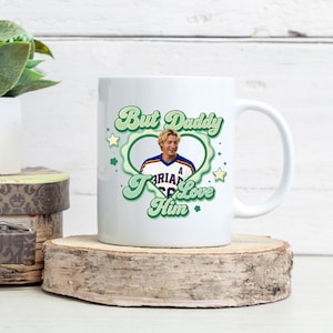 Puede incluir: Taza de cer&aacute;mica blanca con dise&ntilde;o retro. Presenta el texto "But Daddy I Love Him" en verde, una foto de un hombre, estrellas verdes y un marco en forma de coraz&oacute;n.