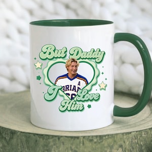 Puede incluir: Taza de cer&aacute;mica blanca con interior y asa verdes. La taza presenta el texto "But Daddy I Love Him" en verde, con una fuente retro, junto con una foto de un hombre dentro de un dise&ntilde;o en forma de coraz&oacute;n verde. Estrellas y tr&eacute;boles decoran el dise&ntilde;o.