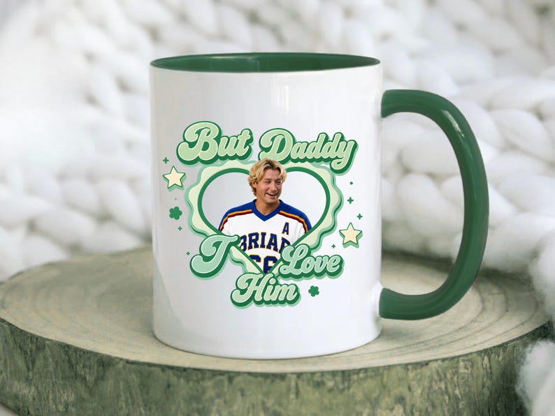 Puede incluir: Taza de cer&aacute;mica blanca con interior y asa verdes. La taza presenta el texto "But Daddy I Love Him" en verde, con una fuente retro, junto con una foto de un hombre dentro de un dise&ntilde;o en forma de coraz&oacute;n verde. Estrellas y tr&eacute;boles decoran el dise&ntilde;o.