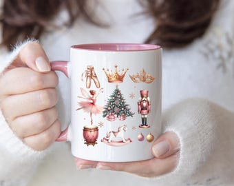 May include: White ceramic mug with a pink rim, featuring a Christmas-themed design with a ballerina, a nutcracker, a Christmas tree, a crown, a mask, a rocking horse, a drum, and a Christmas ornament.
