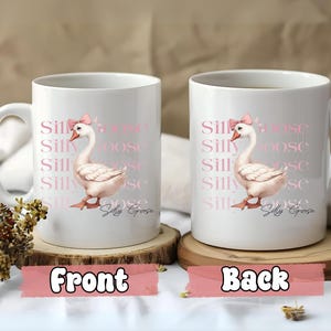 May include: White ceramic mug featuring a pink goose illustration wearing a bow, with the words "Silly Goose" repeated vertically. The mug has a handle and is displayed on a wooden coaster.