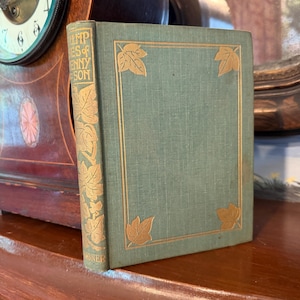 May include: A sage green hardcover book with gold leaf detailing on the front cover and spine. The front cover features a rectangular border with gold leaf ivy leaves at each corner. The spine displays gold text reading Poems of Tennyson.