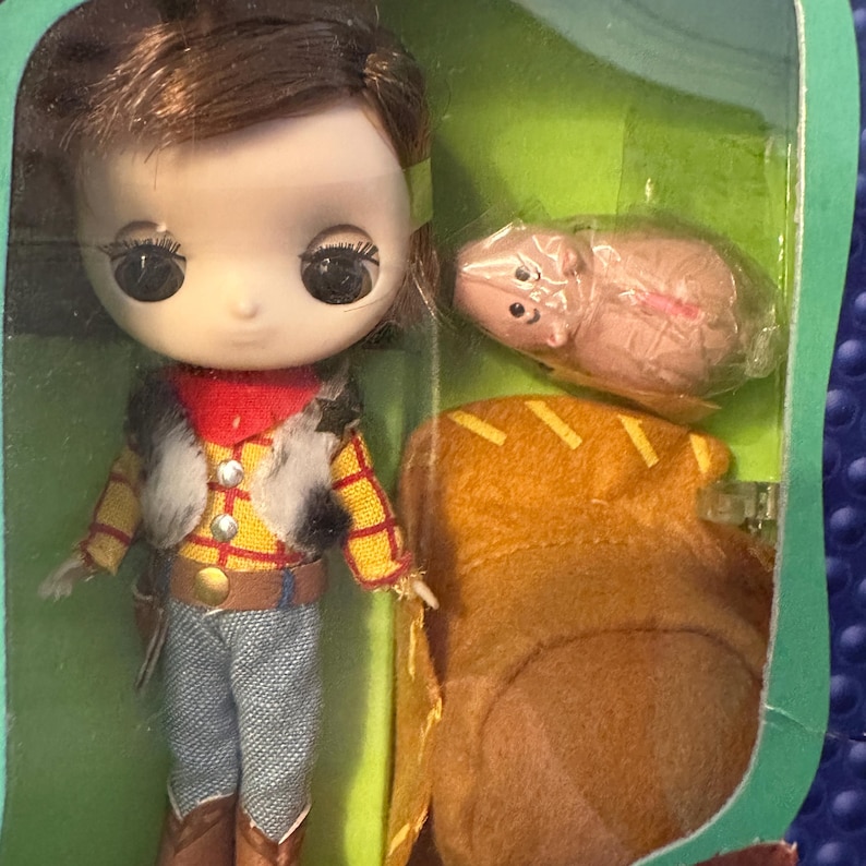 May include: A doll of a character from the animated film Toy Story, wearing a yellow plaid shirt, blue jeans, and a red bandana. The doll is packaged with a small pig figure and a brown saddle.