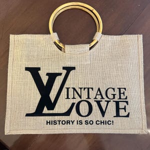 May include: A rectangular burlap tote bag with bamboo handles. The bag features the words "VINTAGE LOVE" in black block letters, with the phrase "HISTORY IS SO CHIC!" below.