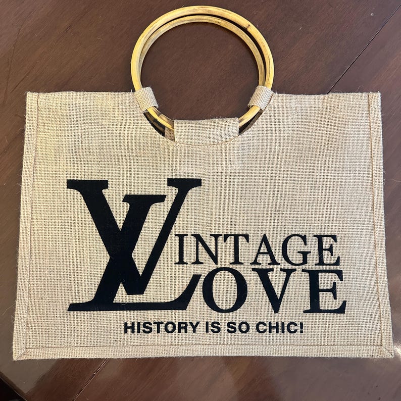 May include: A rectangular burlap tote bag with bamboo handles. The bag features the words "VINTAGE LOVE" in black block letters, with the phrase "HISTORY IS SO CHIC!" below.