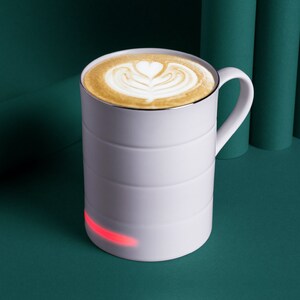 May include: A white mug with a latte art design on top. The mug has a red light on the bottom.