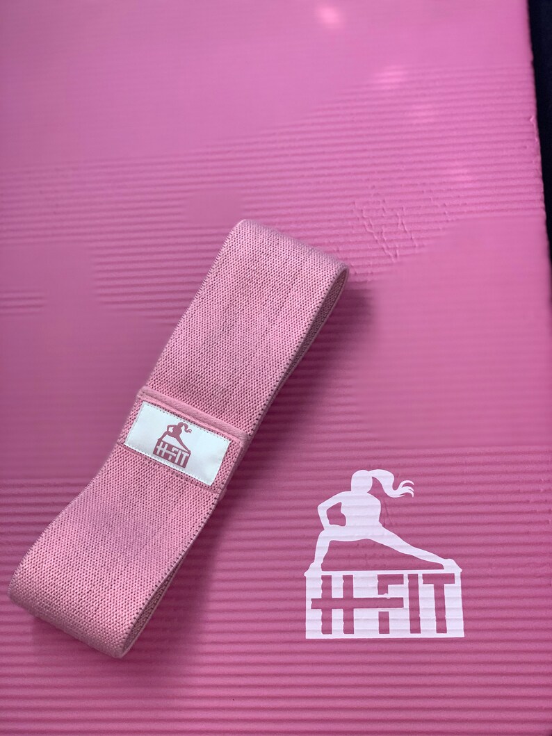 May include: A pink exercise mat with a pink resistance band and a white logo that says "H-Fit" with a silhouette of a woman exercising on top of the text.