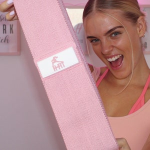 May include: Pink fabric resistance band with a white logo that says "HFit" on it. The band is being held by a person.