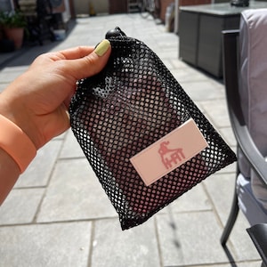 May include: Black mesh drawstring bag with a pink fabric insert. The insert has a white logo with a pink silhouette of a person doing a yoga pose and the text "HHIT".