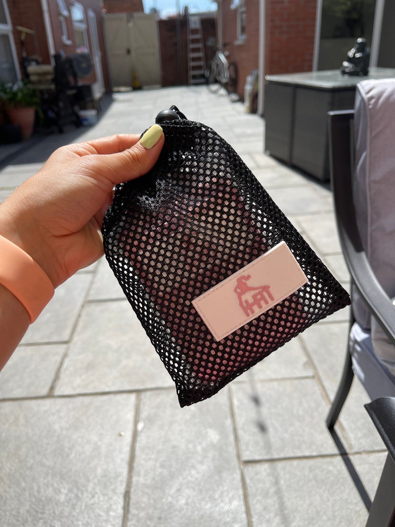 May include: Black mesh drawstring bag with a pink fabric insert. The insert has a white logo with a pink silhouette of a person doing a yoga pose and the text "HHIT".