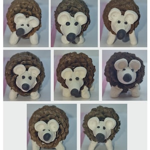 May include: Nine brown pine cones with white clay mouse heads and black noses. The mice have white ears and are facing forward. The pine cones are arranged in three rows of three.