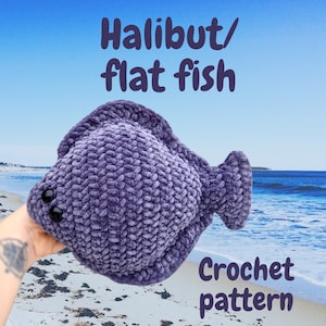 May include: A plush, purple crocheted halibut or flat fish toy with black button eyes. The image includes the text "Halibut/flat fish" and "Crochet pattern" in purple. The background shows a beach and ocean.