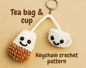 May include: A handmade crochet keychain featuring a tea bag and teacup design. The tea bag is white and brown, and the teacup is white. Both have smiling faces with black eyes. The text "Tea bag & cup" and "Keychain crochet pattern" are also visible.