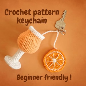 Può includere: Portachiavi con motivo all'uncinetto raffigurante una fetta d'arancia e un bicchiere da cocktail, entrambi nei toni dell'arancione e del bianco. Il portachiavi è attaccato a una chiave. Il testo sull'immagine recita "Crochet pattern keychain" e "Beginner friendly!"