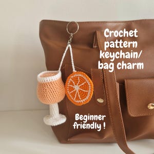 Può includere: Un set di portachiavi e ciondoli per borse all'uncinetto con un bicchiere da cocktail e una fetta d'arancia. Il bicchiere è color pesca con bordo e base bianchi. La fetta d'arancia è arancione con dettagli bianchi. Il testo dice "Crochet pattern keychain/ bag charm" e "Beginner friendly!"