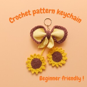 Może przedstawiać: Szydełkowy brelok do kluczy z żółto-brązową kokardą i dwoma żółto-brązowymi słonecznikami. Tekst brzmi "Crochet pattern keychain" i "Beginner friendly!"