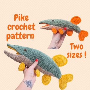 Może przedstawiać: Dwa szydełkowe szczupaki w różnych rozmiarach. Ryby są zielone, pomarańczowe i żółte. Tekst "Pike crochet pattern" i "Two sizes!" jest pomarańczowy.