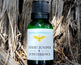 May include: A green glass bottle with a black cap and a white label that reads "Spiritual Performance Desert Juniper Quintessence". The bottle is sitting on a brown, textured surface.
