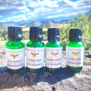 Könnte beinhalten: Vier kleine grüne Glasflaschen mit schwarzen Kappen, jede mit einem anderen ätherischen Öl. Die Flaschen sind mit den Namen "Blue Spruce", "Desert Sage", "Desert Juniper" und "Piñon Pine" sowie dem Text "Spiritual Performance Quintessence" beschriftet.