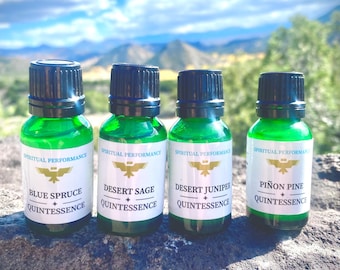 May include: Four small green glass bottles with black caps, each containing a different essential oil. The bottles are labeled with the names "Blue Spruce", "Desert Sage", "Desert Juniper", and "Piñon Pine" and the text "Spiritual Performance Quintessence".