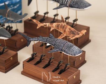 Puede incluir: Esculturas de tiburones de madera articulada montadas sobre bases rectangulares de nogal con varillas metálicas. Cada tiburón presenta detalles pintados a mano, incluyendo puntos blancos sobre cuerpos oscuros. La base muestra el texto Nick's Wood Art.
