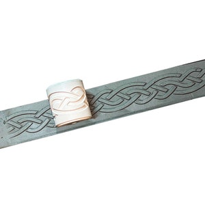 May include: A white rubber stamp with a Celtic knot design. The stamp is on a grey surface with the same design.