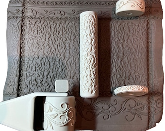 May include: A set of three white rolling pins with intricate floral designs. The rolling pins are on a brown textured surface.