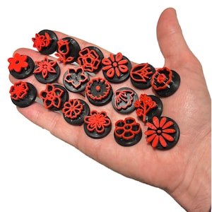 Peut inclure: Ensemble de tampons noirs et rouges en forme de fleurs. Chaque tampon présente un motif floral rouge différent sur une base circulaire noire. Les tampons sont tenus dans une main, montrant la variété des motifs.