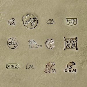 May include: A collection of 10 different stamps or labels, each with a unique design. The stamps feature various symbols, letters, and words, including "AJ", "SMOSS POT", "KRL", "Lee", and "COM".