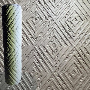 May include: A green and white textured paint roller with a diamond pattern. The roller is on a background of a textured surface with a diamond pattern.
